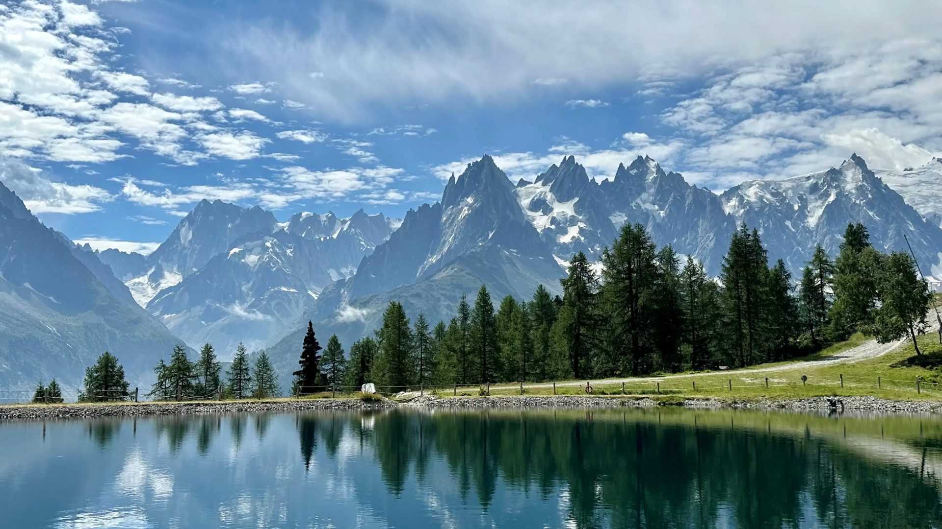Idyllische Ansicht eines kristallklarem Bergsee vor dem Panorama schneebedeckter Berge, reflektiert unter einem blauen Wolkenhimmel, betont die Bedeutung des Klimaschutzes in einem nachhaltigem unternehmen.